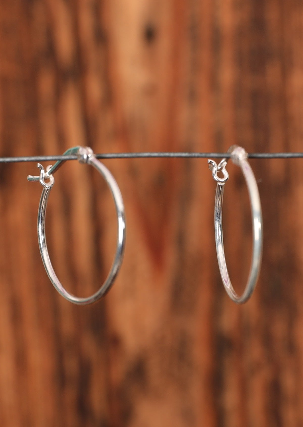 92.5% silver slim hoop earrings sitting on a wire for display.