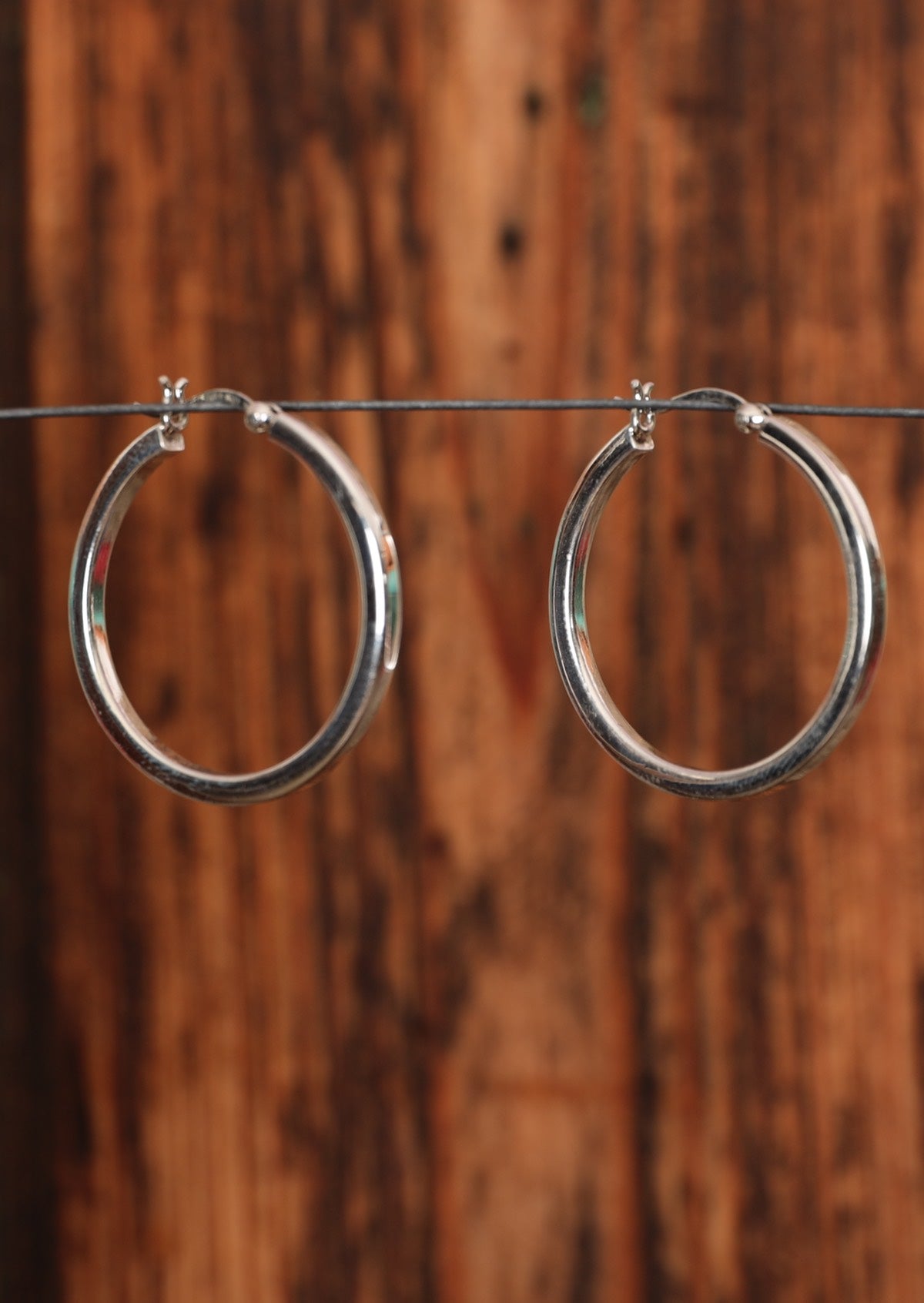 92.5% silver chunky hoop earrings sitting on a wire for display.