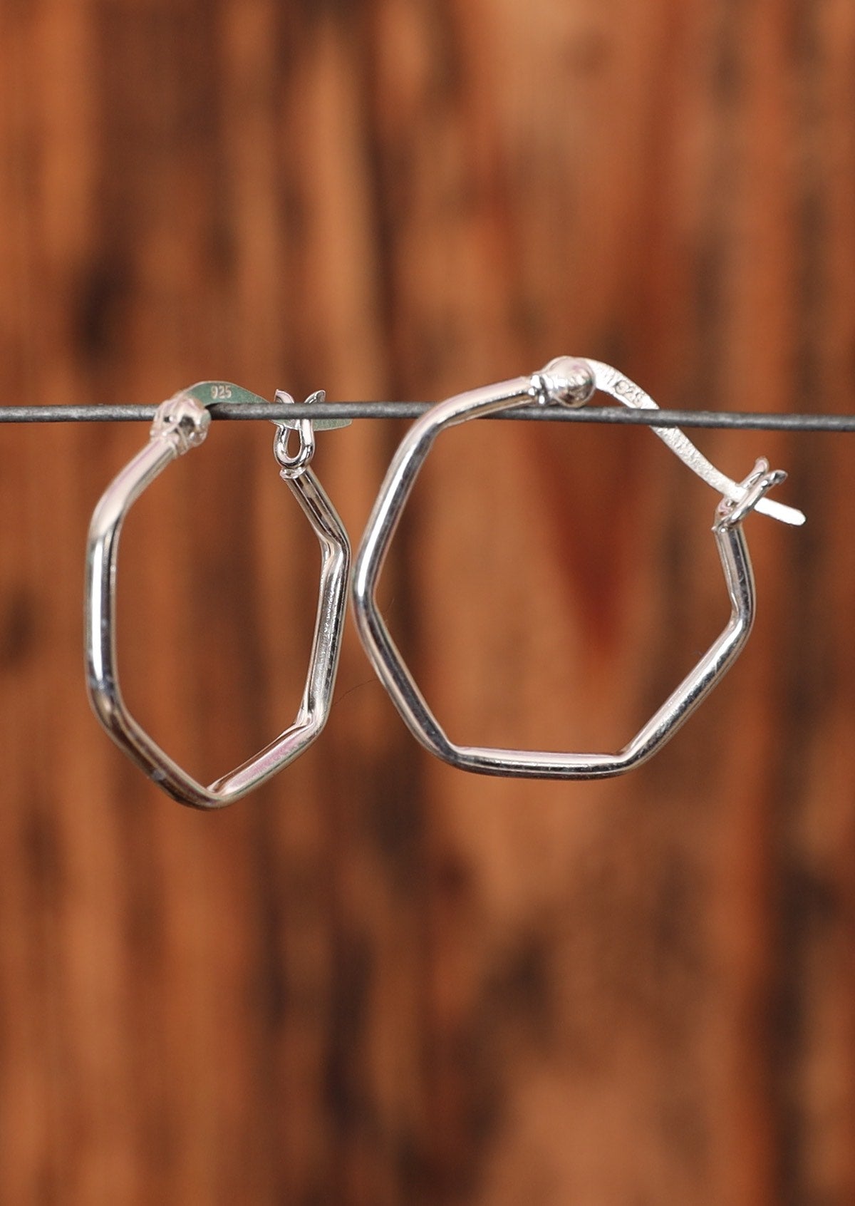 92.5% silver hoop earrings in a hexagonal shape sitting on wire for display.