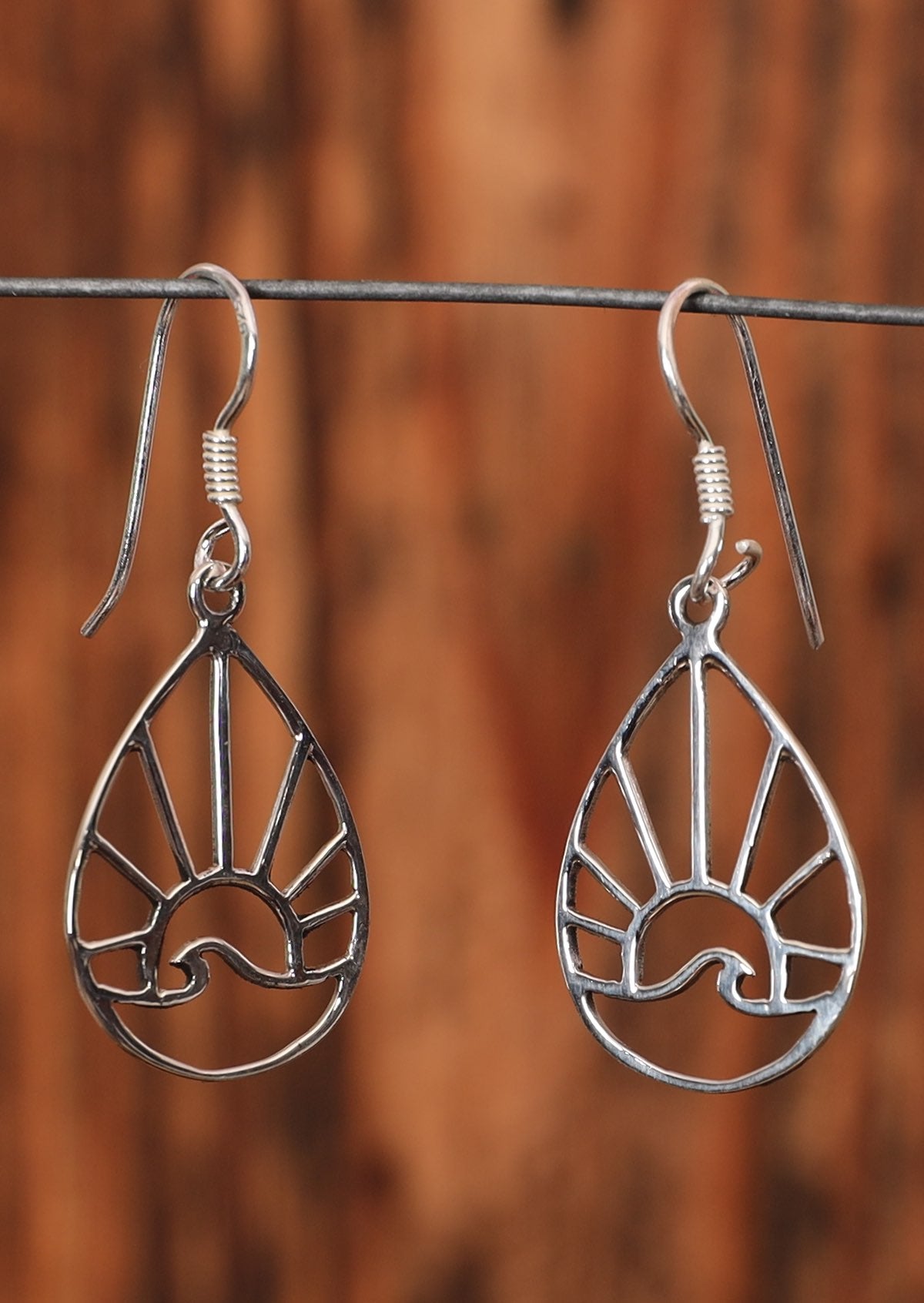 These 92.5% silver earrings are a teardrop shape with a sun and wave within it. The earrings sit on a wire for display.