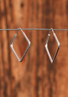 92.5% silver slim diamond shaped hoop earrings sit on a wire for display.