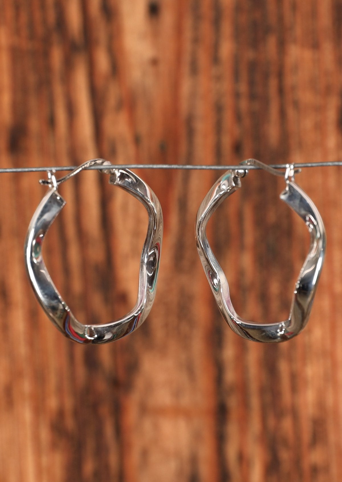 92.5% silver wavy hoops hanging on a wire for display.