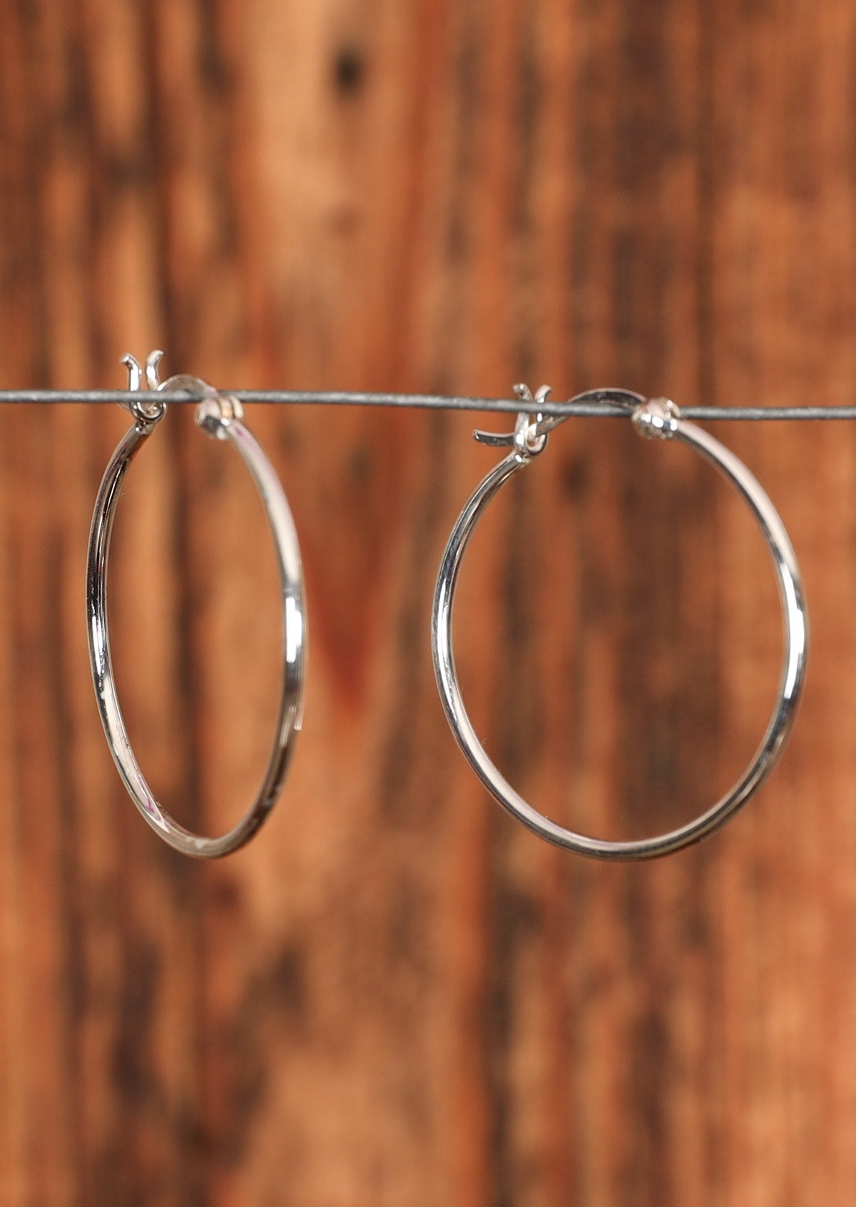 92.5% Slim Silver Hoop earrings sit on a wire for display.