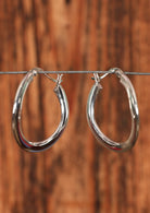 92.5% subtle wave silver hoop earrings sitting on a wire for display