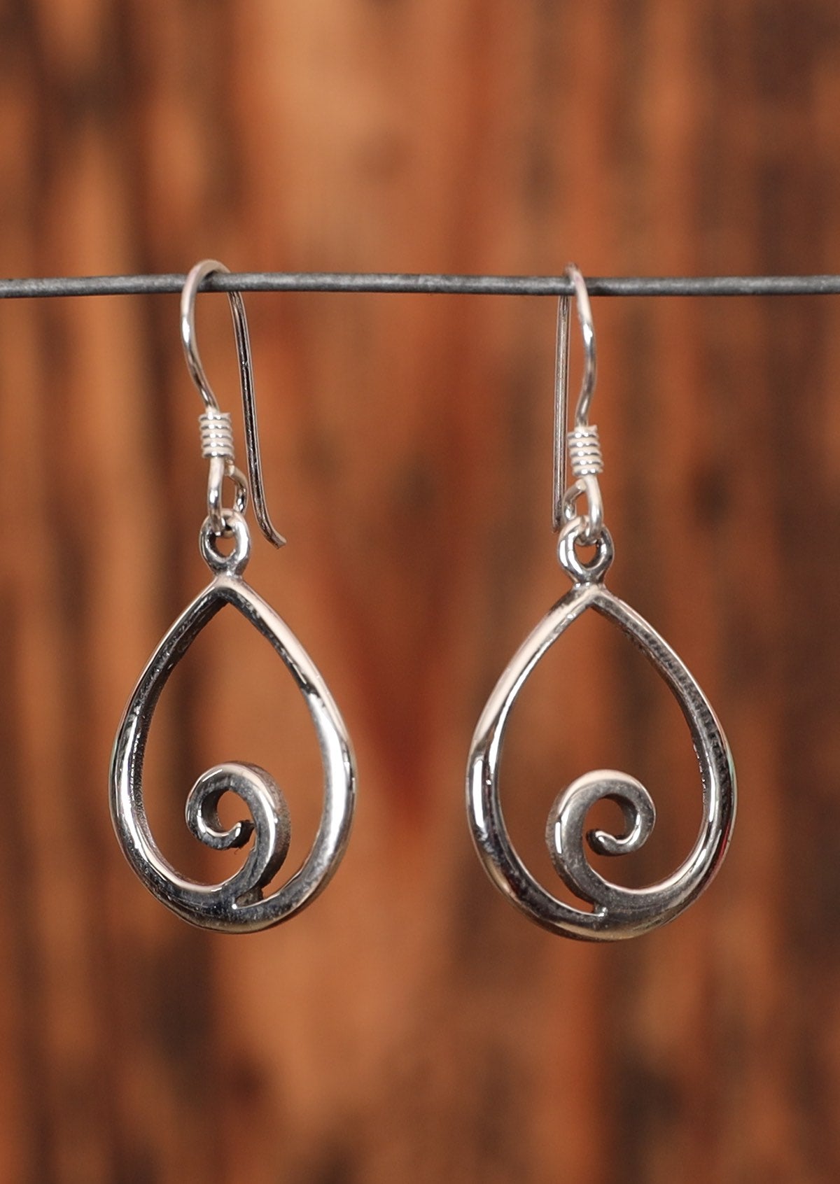 92.5% silver teardrop earrings with a swirl at the bottom sit on wire for display.