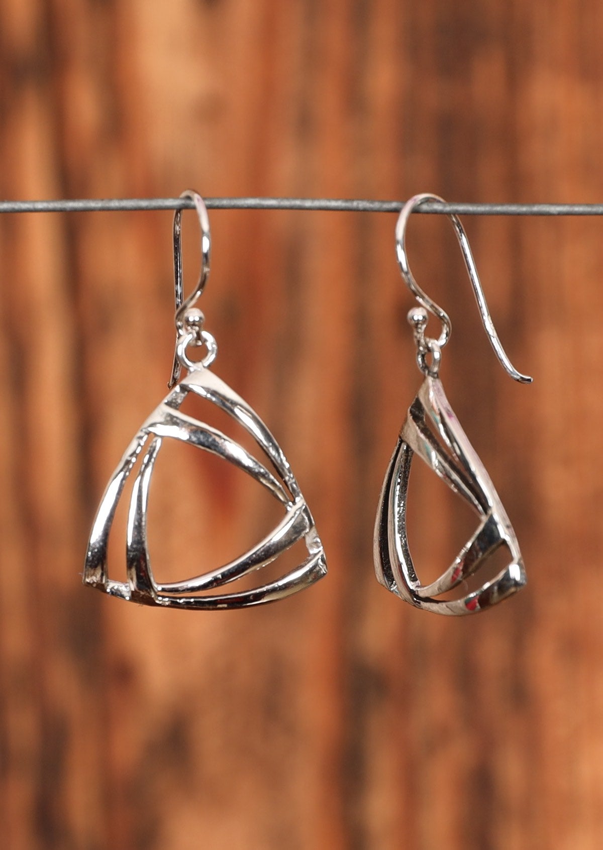 92.5% silver triangle earrings sit on a wire for display.