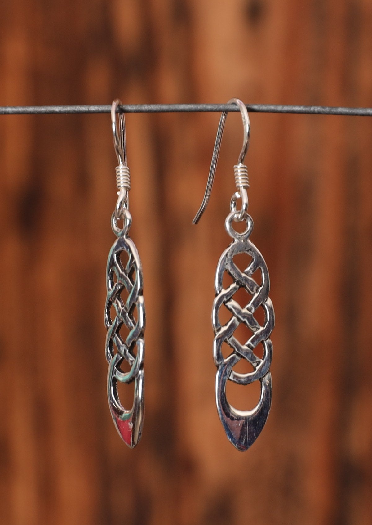 92.5% silver woven braid silver earrings sit on a wire for display.