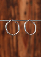 92.5% silver angular hoop earrings sit on a wire for display.