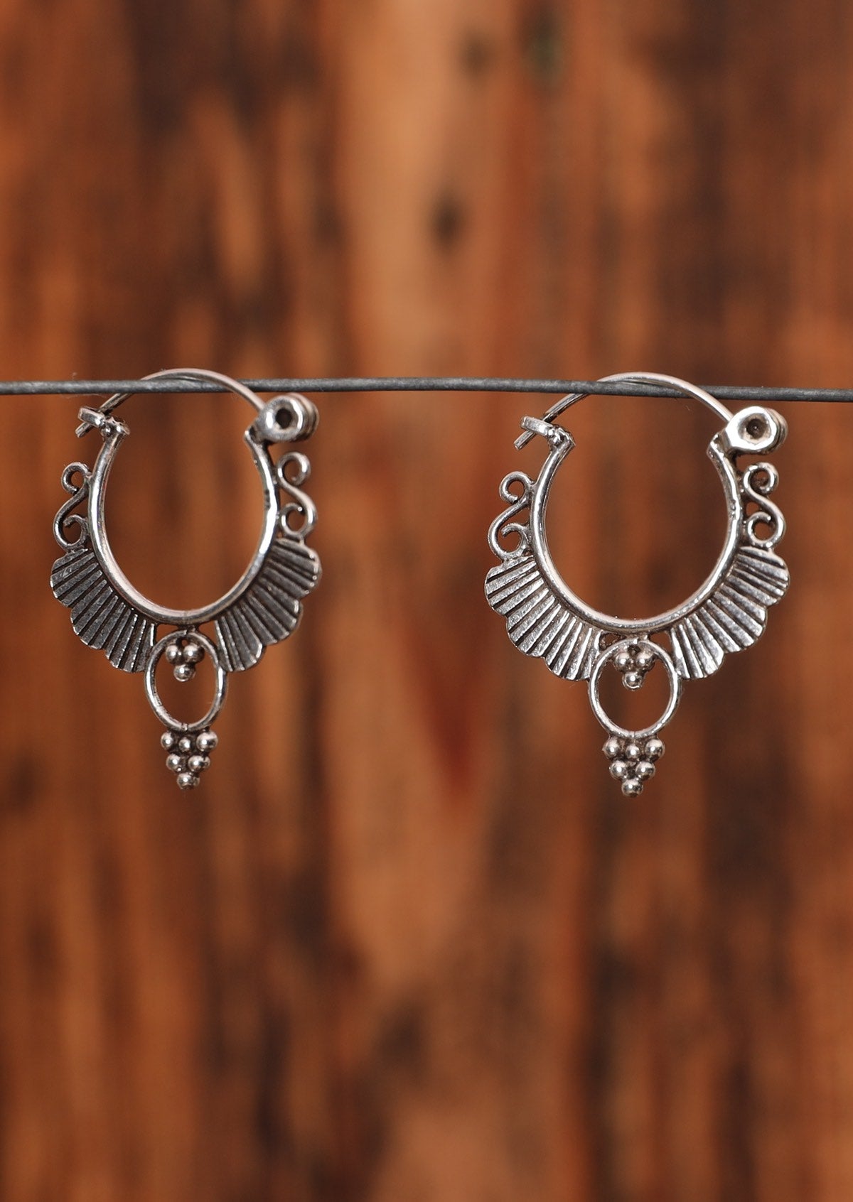 92.5% silver circular ornate earrings hanging on a wire for display.