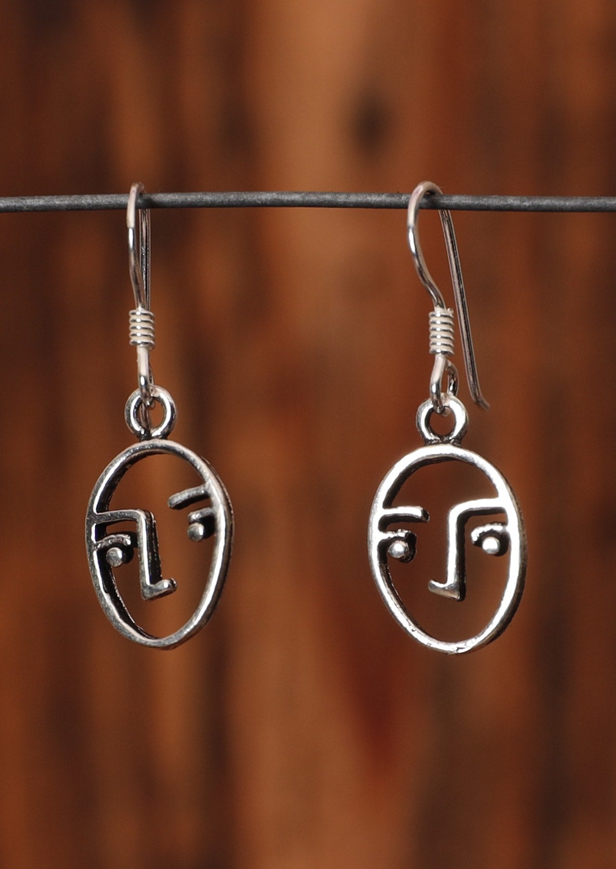 92.5% silver earrings with line drawn faces sitting on wire for display.