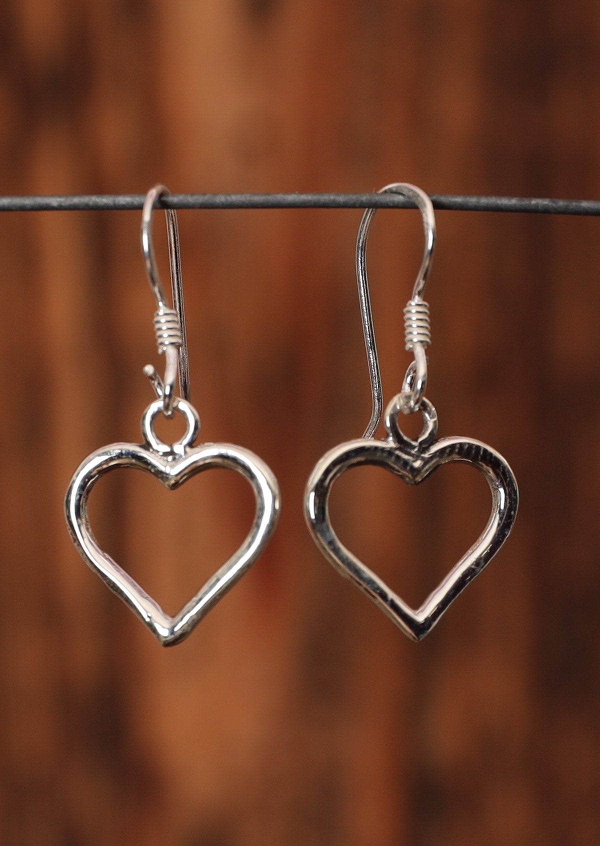 92.5% silver heart shaped earrings with hooks on a wire for display.