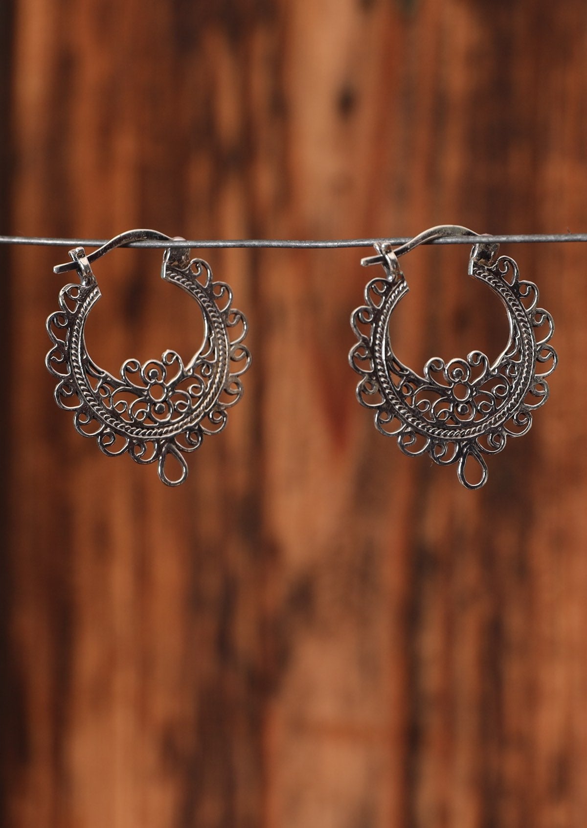 92.5% silver ornate hoops sit on a wire for display.