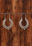 92.5% silver lace style hoop earrings sit on a wire for display.