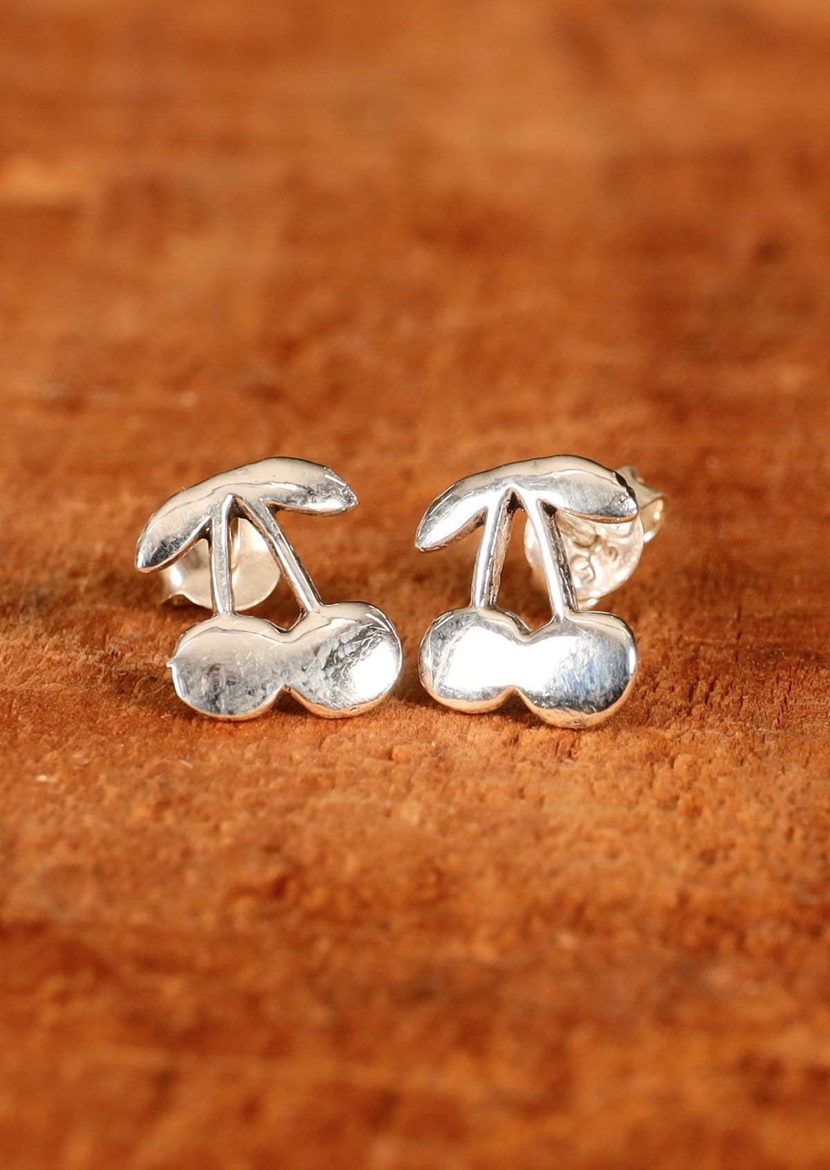 92.5% silver cherry shaped earrings on wood for display.