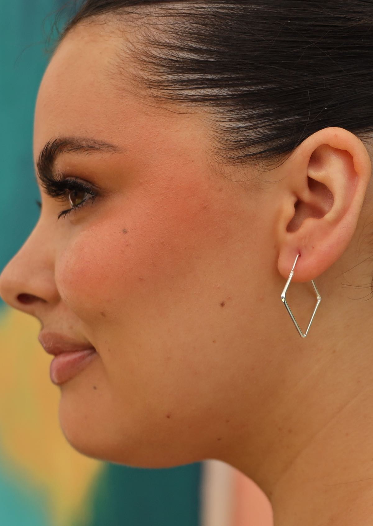 square shaped silver hoop earring on woman with dark hair