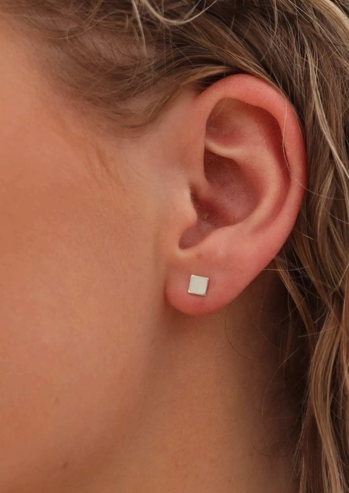 woman's ear with square silver stud earrings