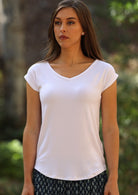 Woman with dark hair wearing a white v-neck short cap sleeve rayon top.