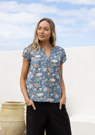 Woman wearing a cotton dusty blue floral print short sleeve blouse with V-neckline and elastic ruching at the front of the shoulders