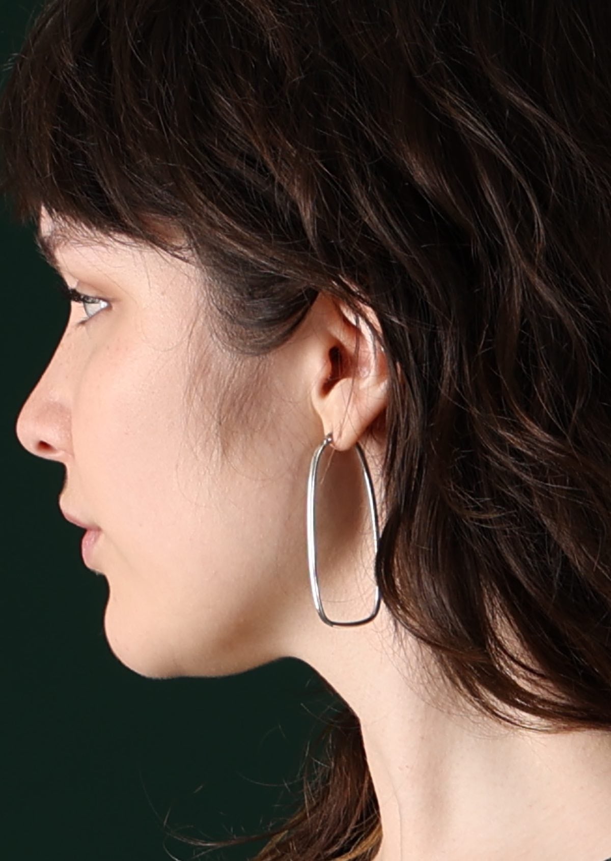 Model with dark hair wearing elongated large  silver hoop earrings 