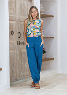 Woman wearing a pastel coloured sleeveless cotton top, tucked into blue pants, with hands in pockets