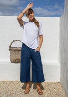 Woman wears deep blue wide leg 3/4 cotton pants with high waist, pockets, side zipper and wide waistband