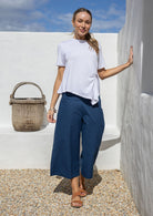 Woman stands in 100% cotton wide leg 3/4 pants in dark sea blue paired with a white rayon basic top 