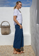 Woman stands sideways wearing a high waisted cotton wide-leg pants in dark blue with hands in pocket