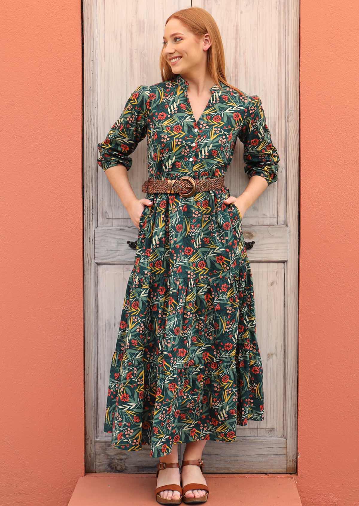 Model stands with her hands in the pockets of her green based, floral print dress. 