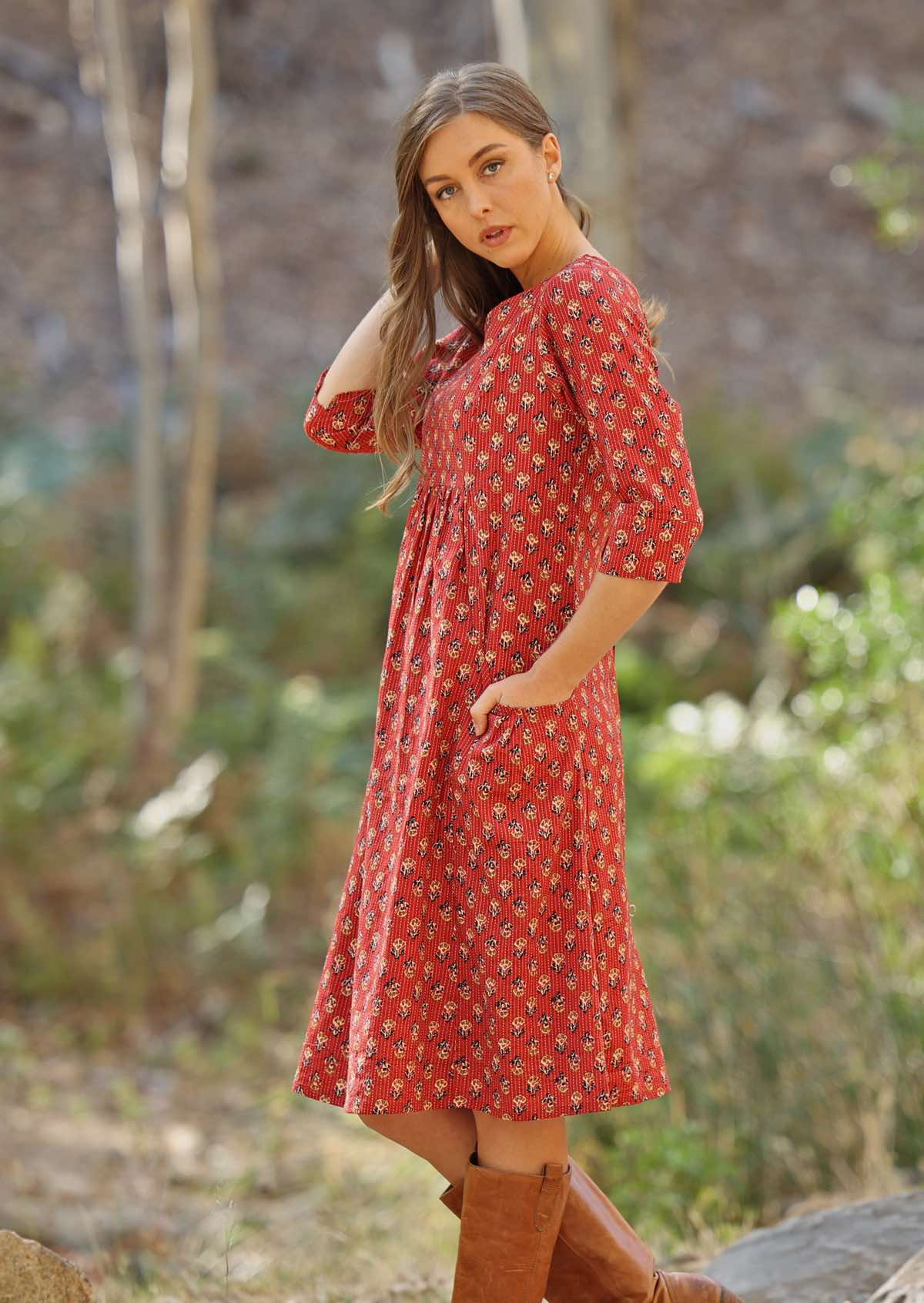 Woman has her hands in the pocket of her red cotton dress. 
