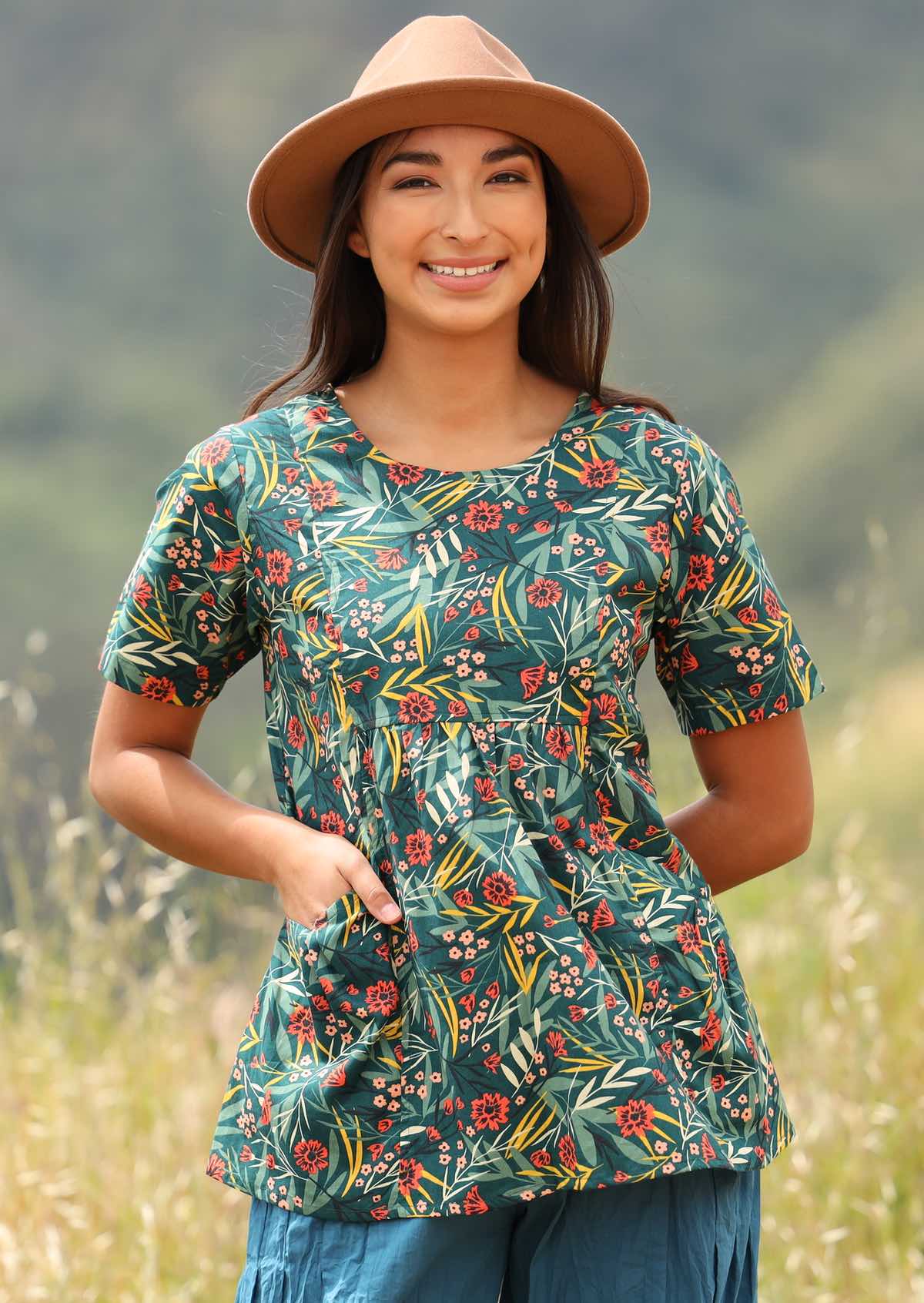 Model wears a loose fitting floral top with a green base. 