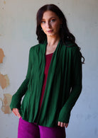 Model wears dark green soft, stretch rayon cardi with long sleeves, open at front to reveal a maroon top underneath 