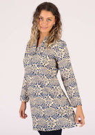 Smiling woman wears a cream based tunic with a blue dahlia print. 