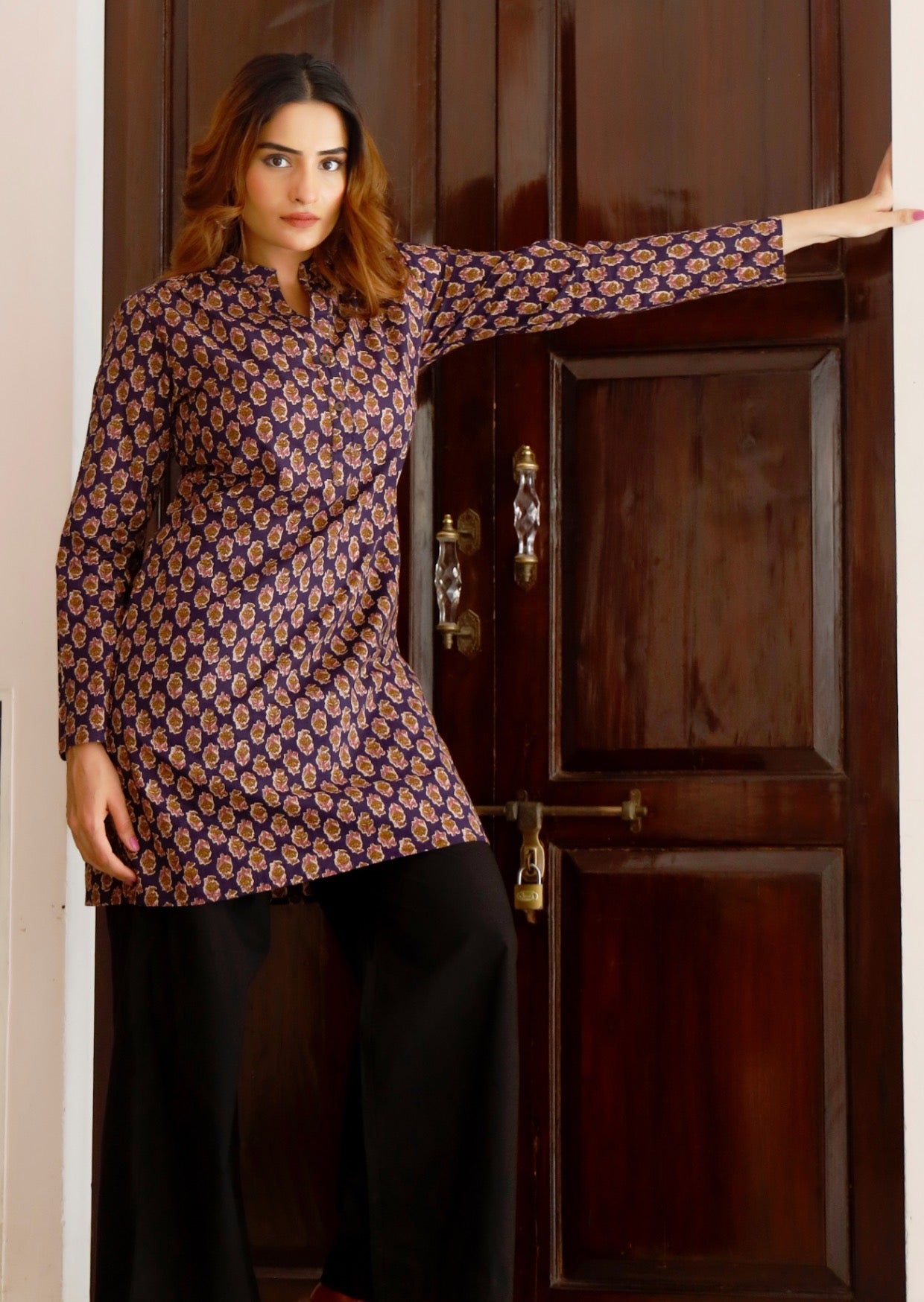 Woman wears cotton long sleeve tunic with two buttons across the bodice and mandarin collar, in dark purple based floral print 