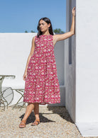 Woman wearing a pink floral cotton midi dress standing against a white wall with blue sky.