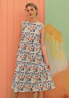 Model wears a knee length floral dress with a white base. 