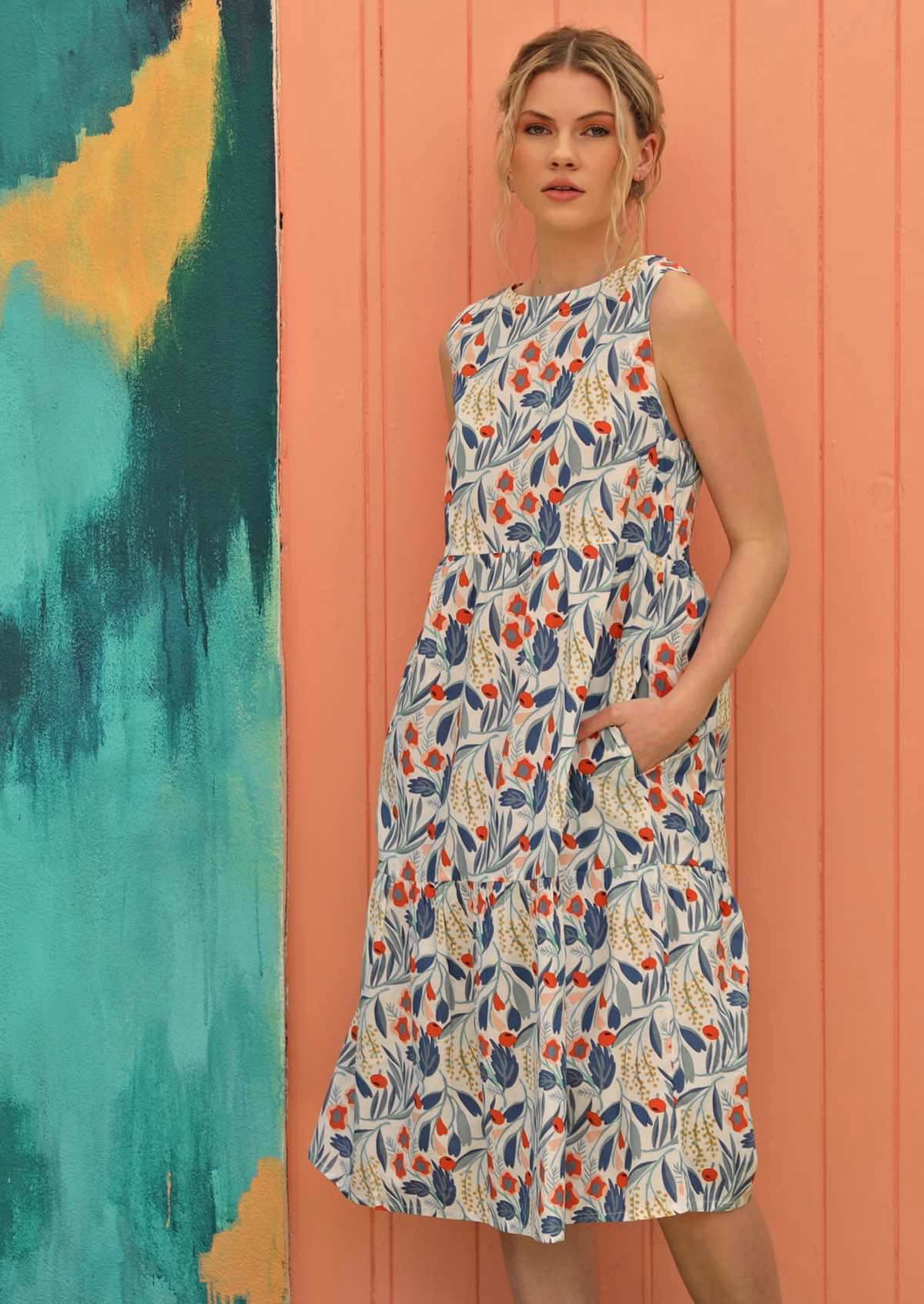 Blonde woman has her hands in the pockets of her relaxed fit, floral dress. 
