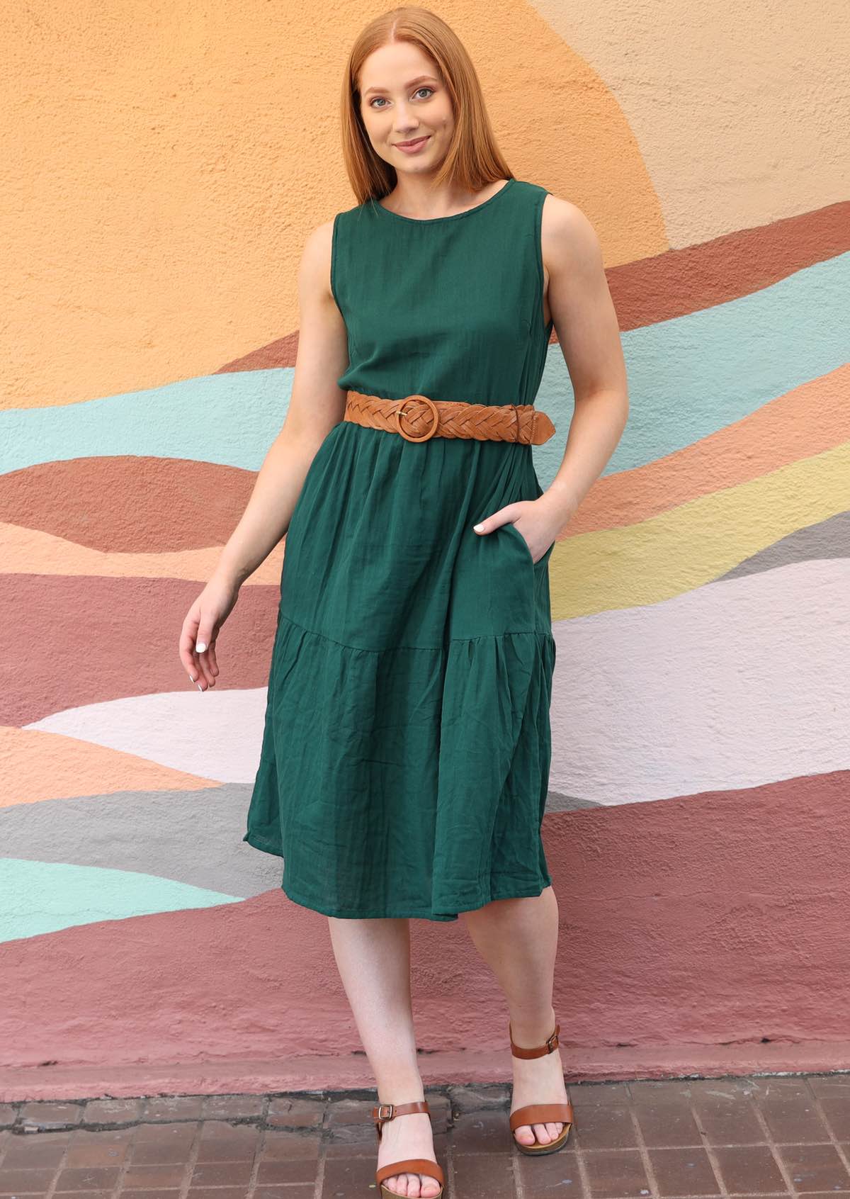 Model wears loose fitting green cotton dress with belt to cinch in the waist. 