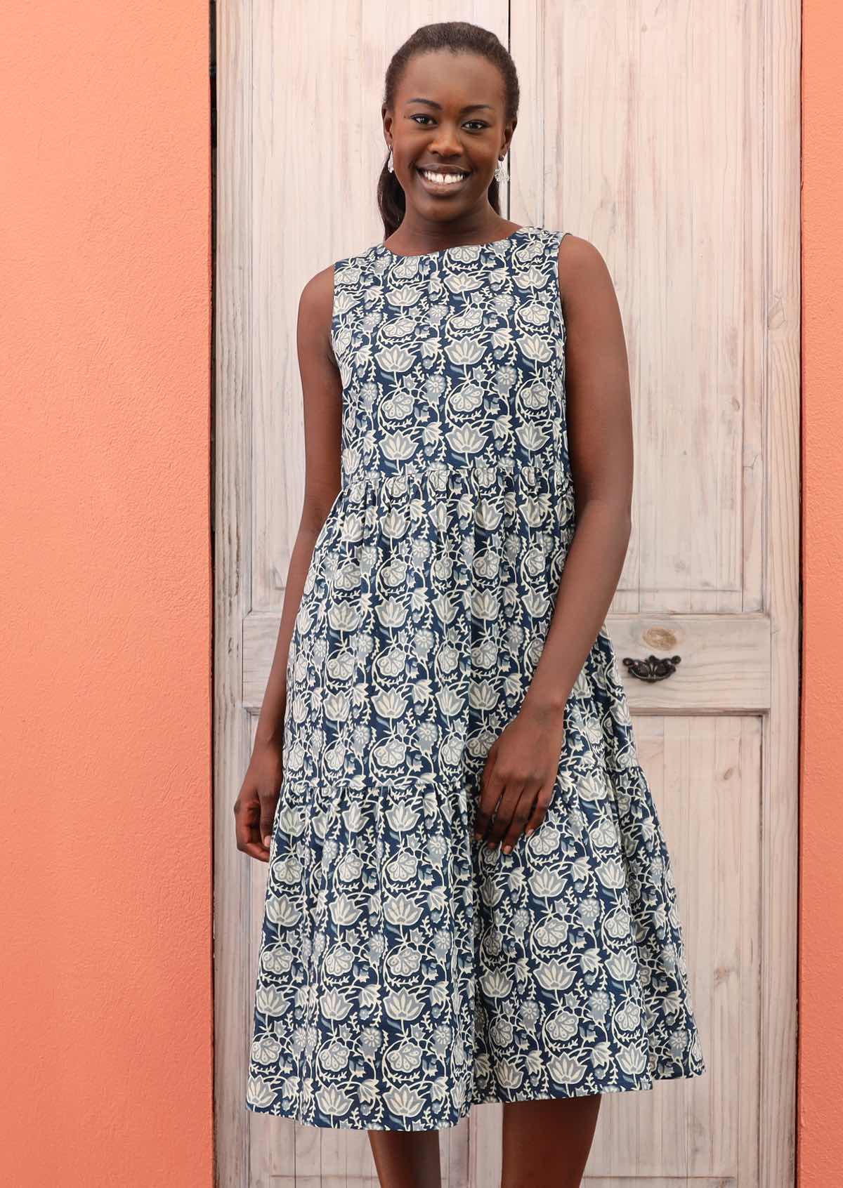 Smiling model wears a blue based dress with a white stamped floral pattern. 