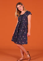 Model standing side on wearing 100 percent cotton short sleeve pleated sundress in deep purple Indian floral