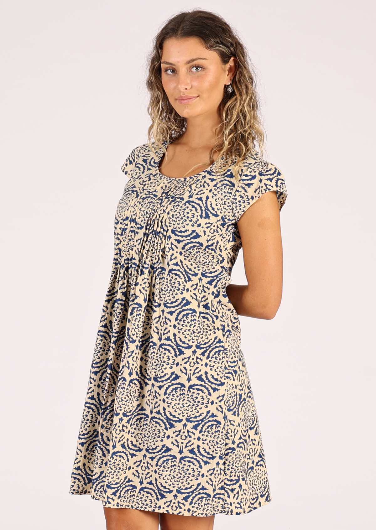 Model wears a cotton dress that sits above the knee, featuring a blue floral print on a cream base. 