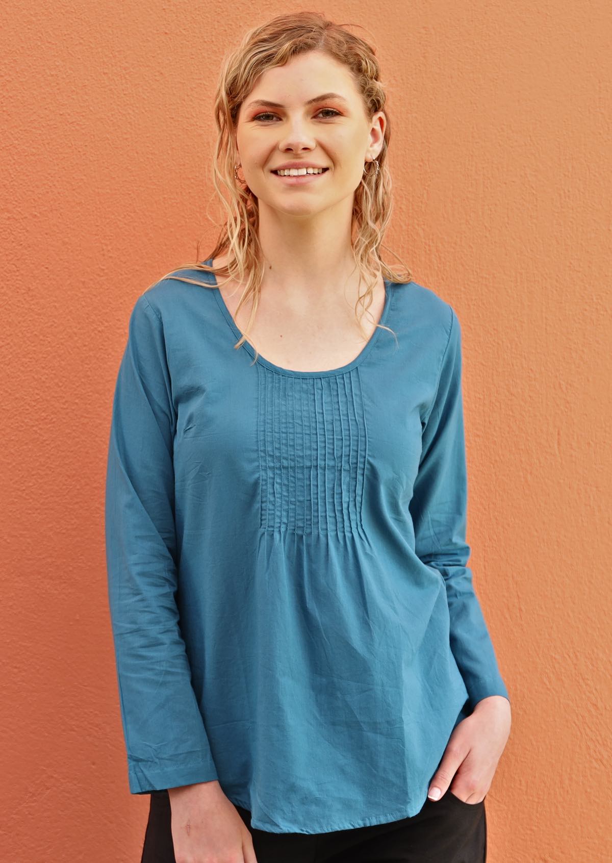 Smiling woman wears a lightweight cotton top that sits below the hip bone. 
