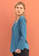 Model wears blue, lightweight cotton top with long sleeves. 