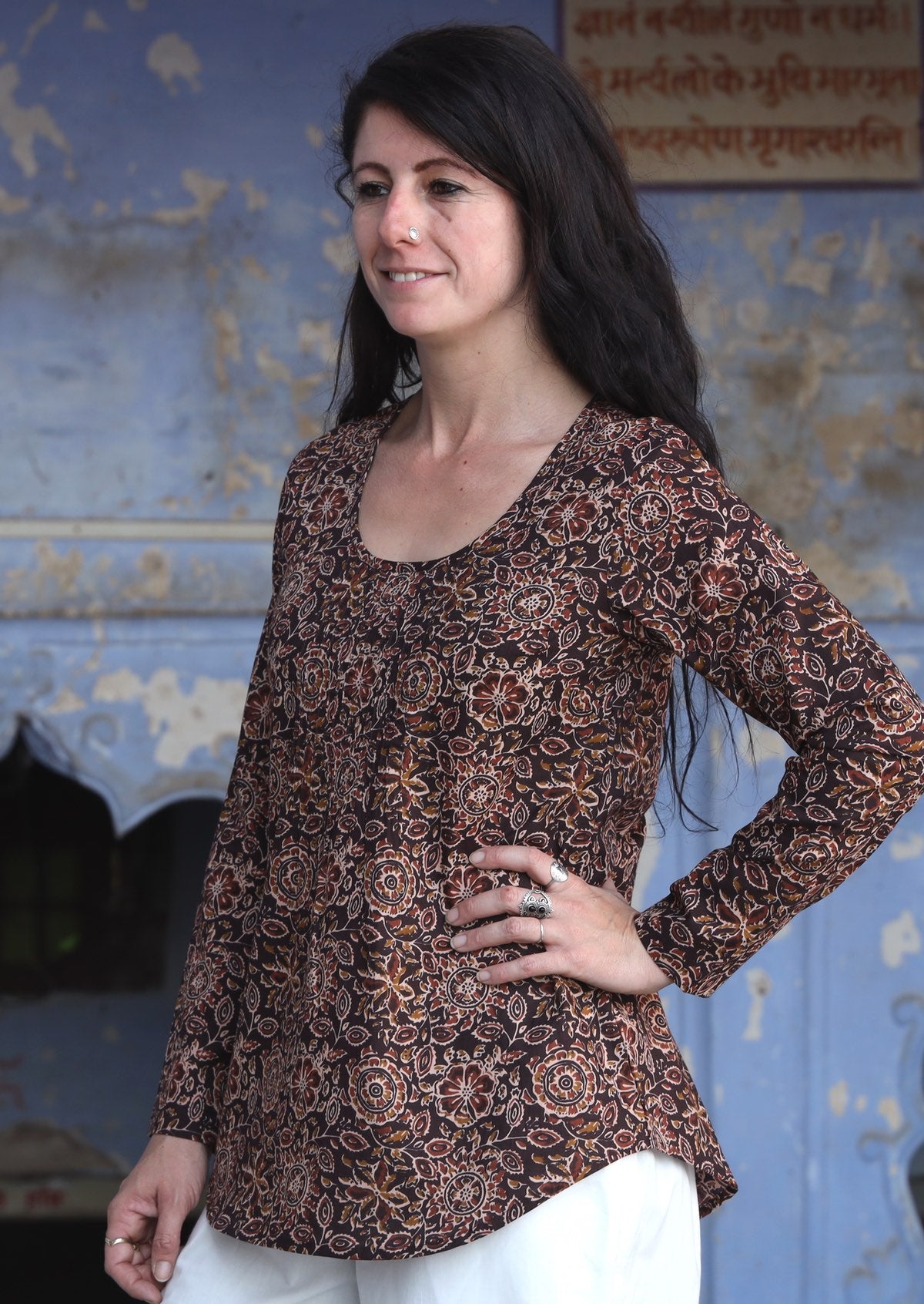 Woman standing sideways with hand on hip wearing 100% cotton long sleeve top with tiny pleated details and round neck.