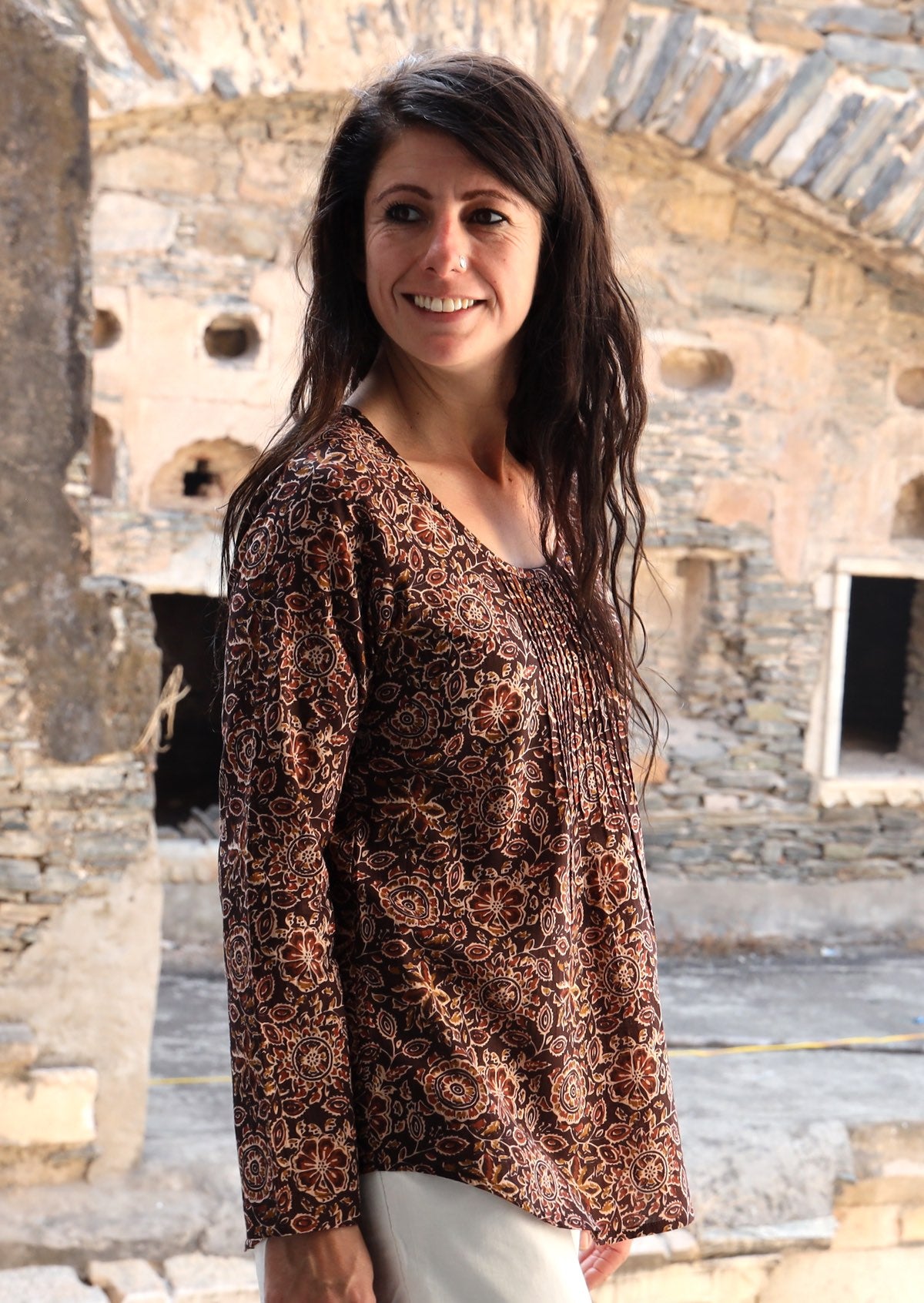 Model looking over her shoulder wearing 100% cotton long sleeve top with round neckline and tiny pleat detail from the center of the neckline.
