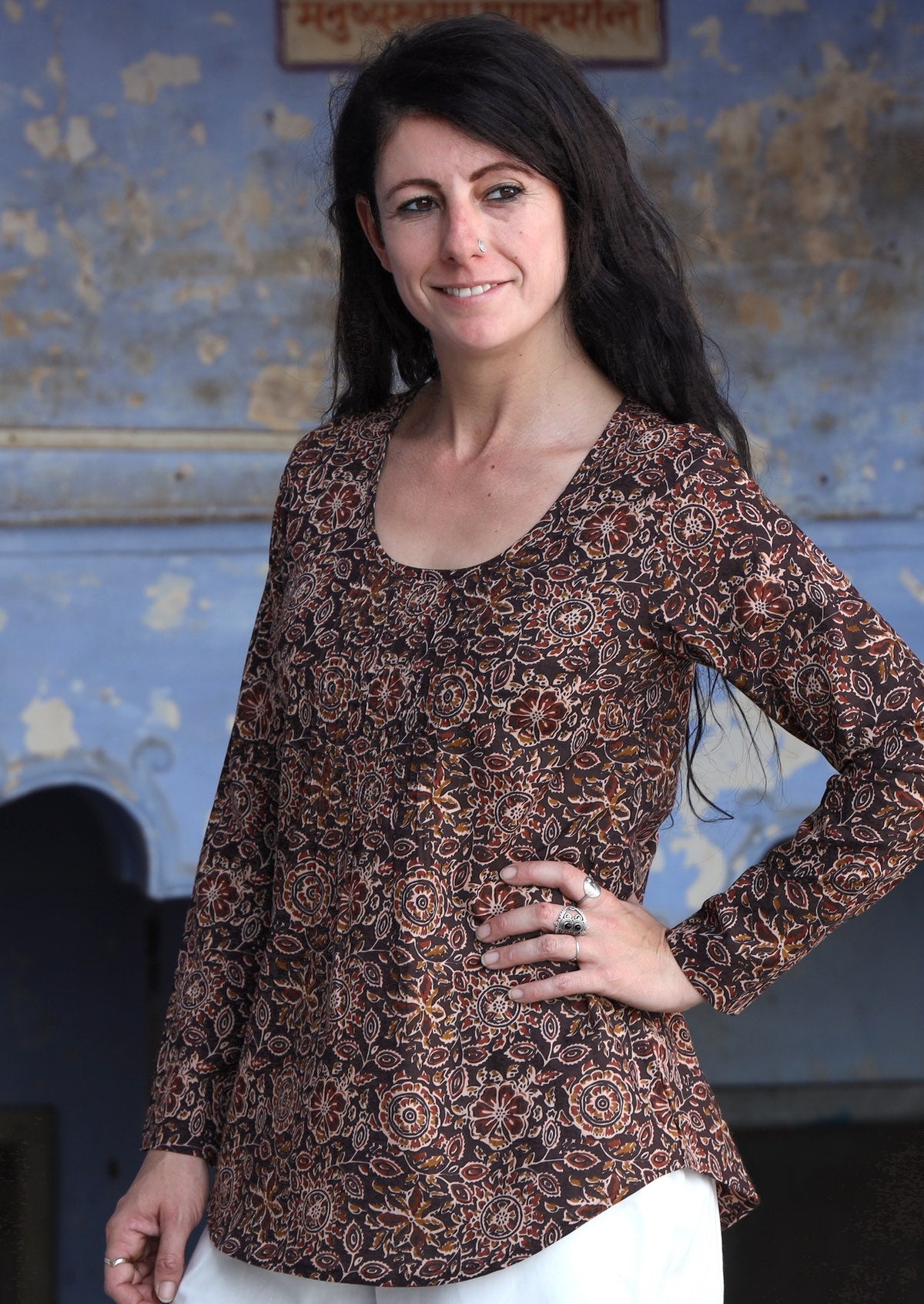 Model wearing 100% cotton long sleeve top in brown with round neckline and tiny pleat detail from the center of the neckline.