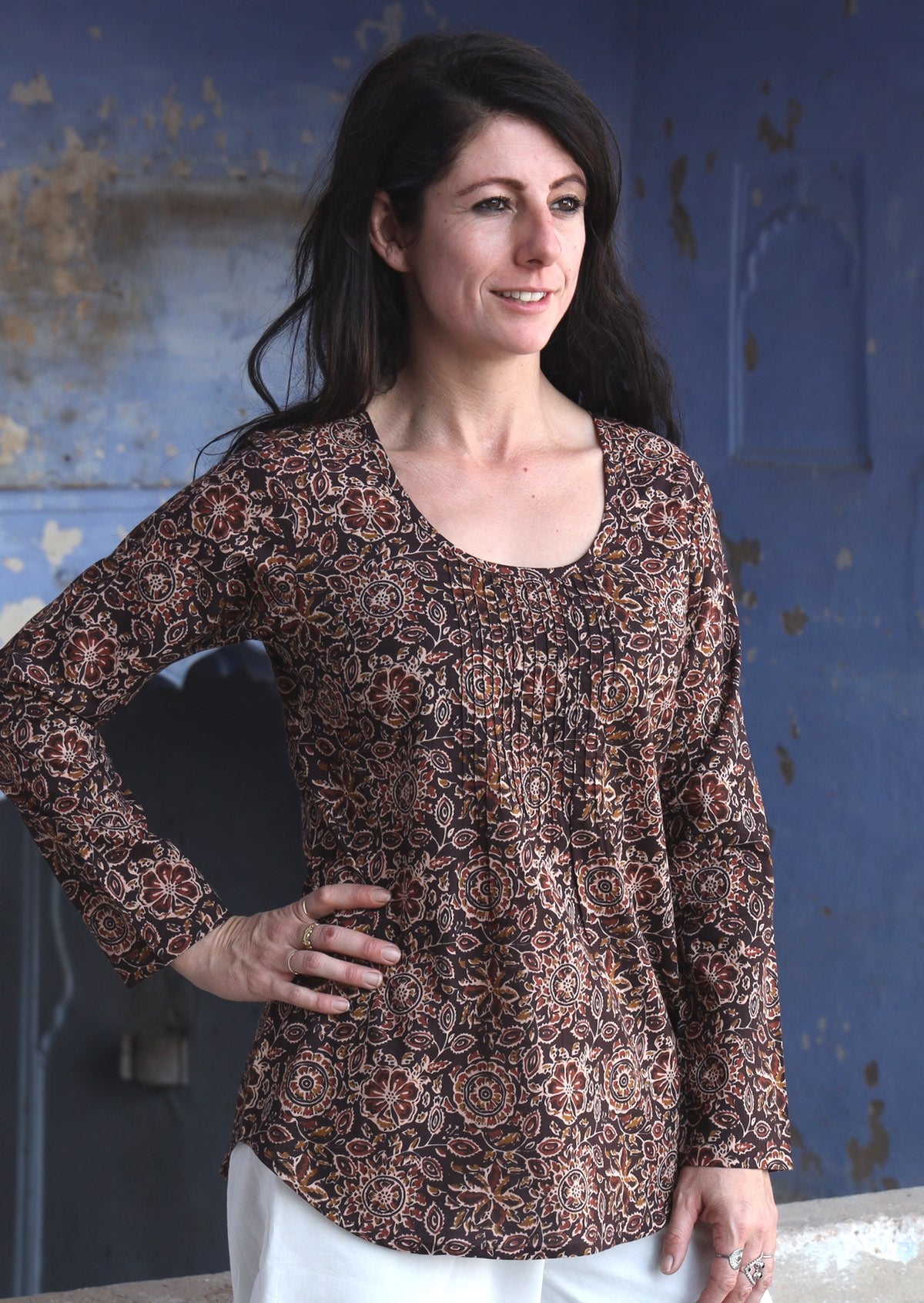 Model wearing 100% brown based floral cotton long sleeve top with round neckline and tiny pleat detail from the center of the neckline.