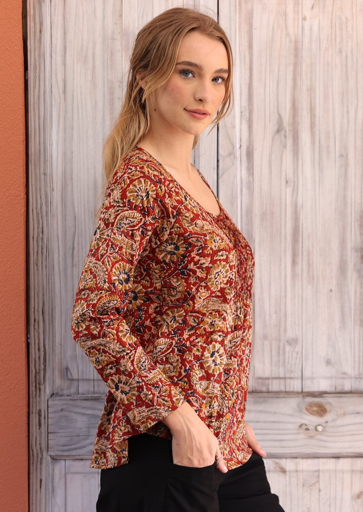 Woman wearing long sleeve earthy toned Indian print cotton blouse with black cotton pants hands in pockets 