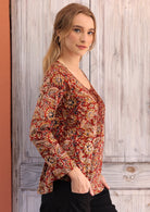 Woman wearing long sleeve earthy toned Indian print cotton blouse with black cotton pants hands in pockets 