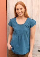 Model wears a short sleeve top with small decorative pleats on the bust. 