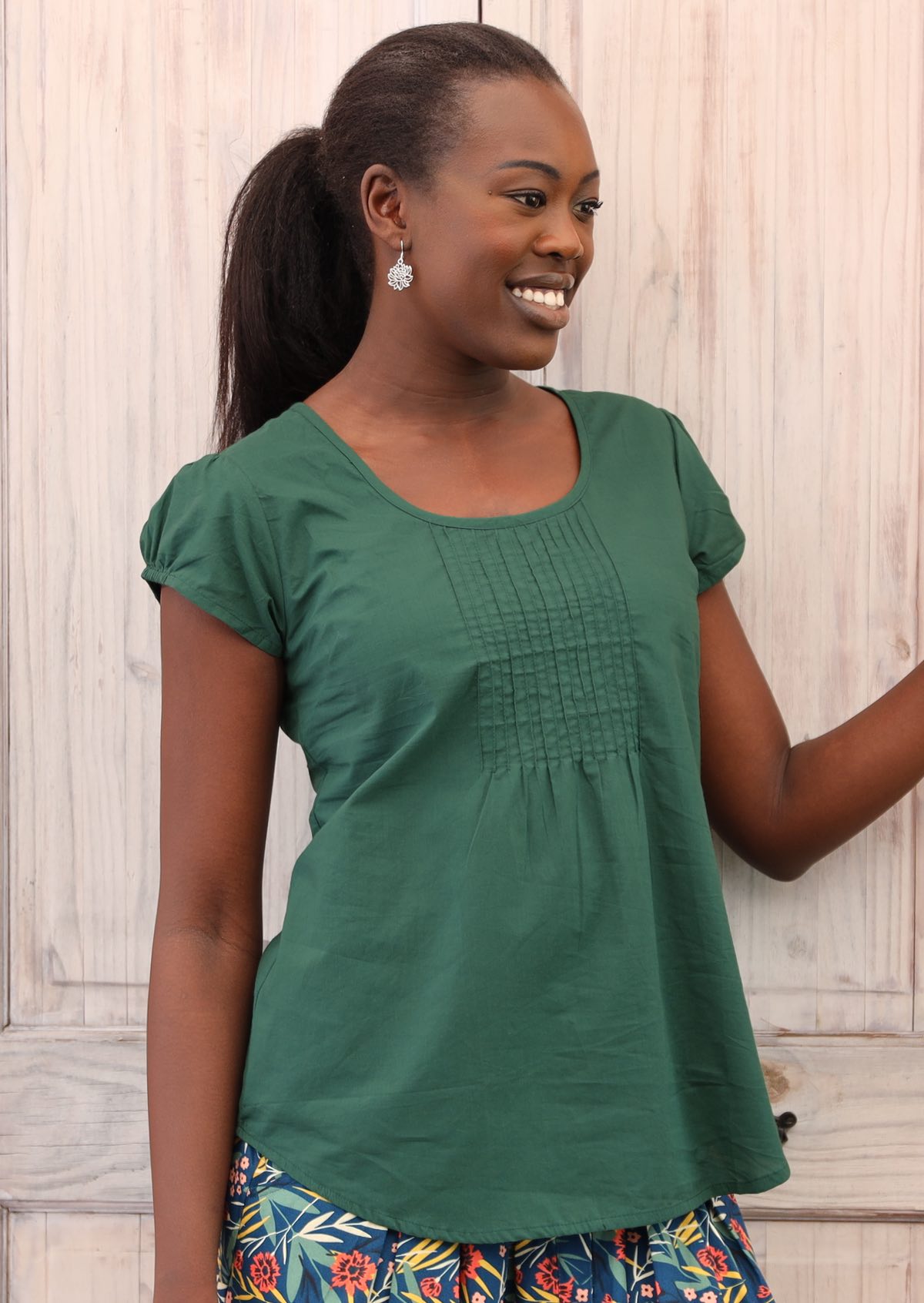 Smiling model wears a green top with small decorative pleats on the bust. 